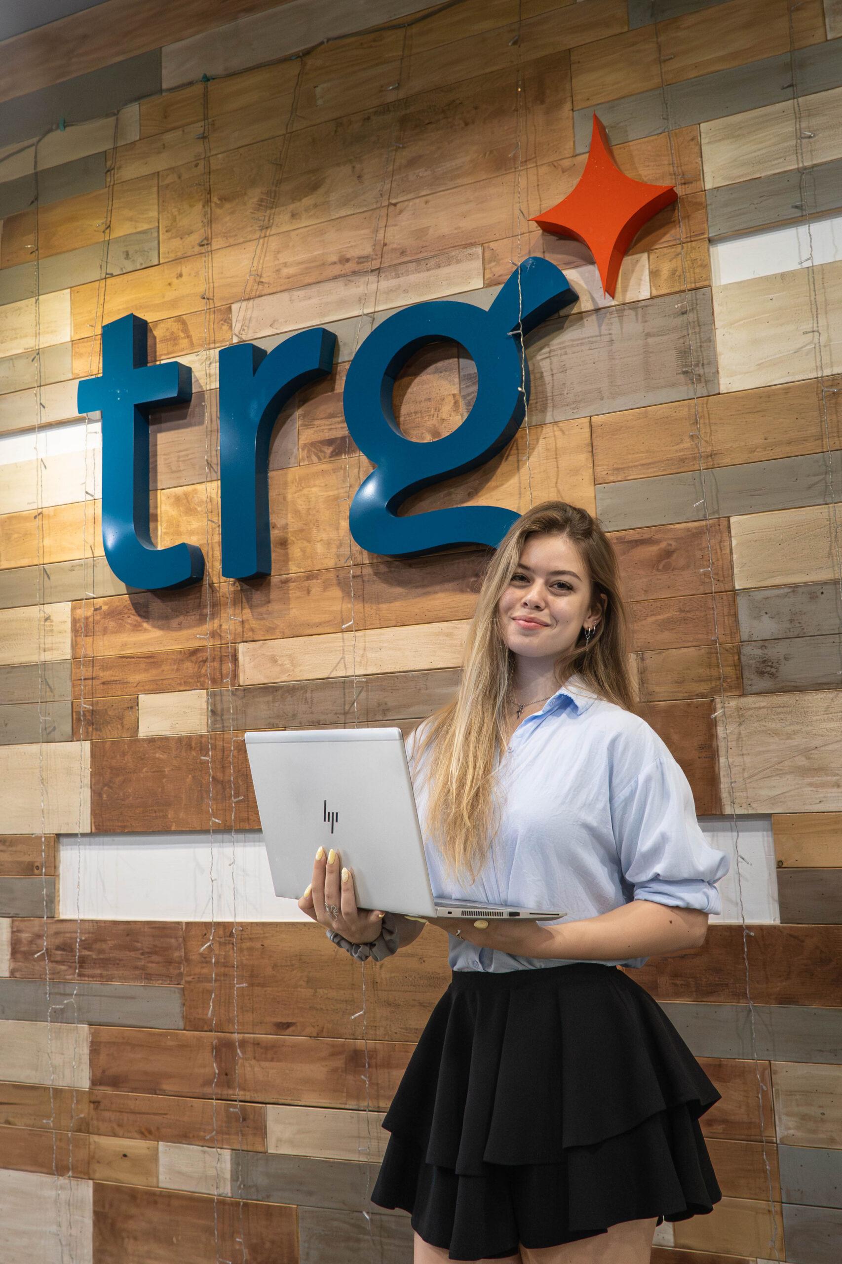 A TRG intern holding a laptop in front of the TRG wall
